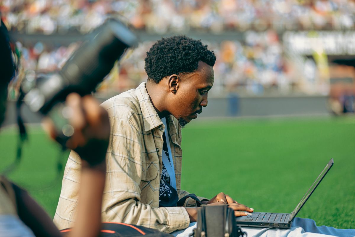 A photographer working on a laptop with a camera at an outdoor event.